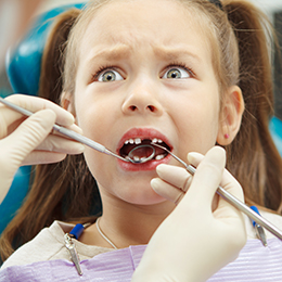 Scared child sits at dentist chair with open mouth